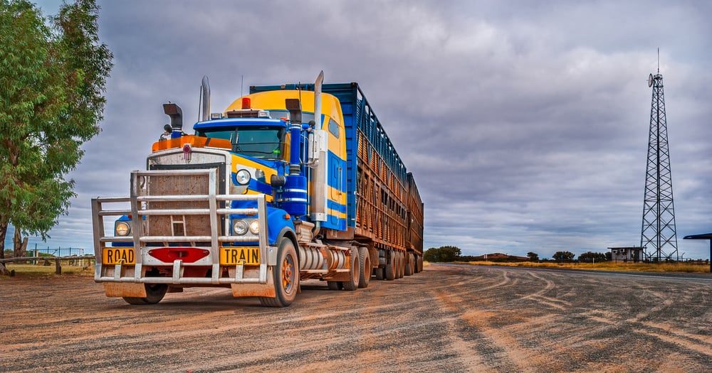 A road train specialized for transporting livestock, parked on a dirt lot beneath a moody, overcast sky.